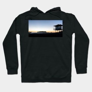 Silhouetted against golden glow of sunrise lifesafers lookout on Mount Maunganui beach New Zealand. Hoodie